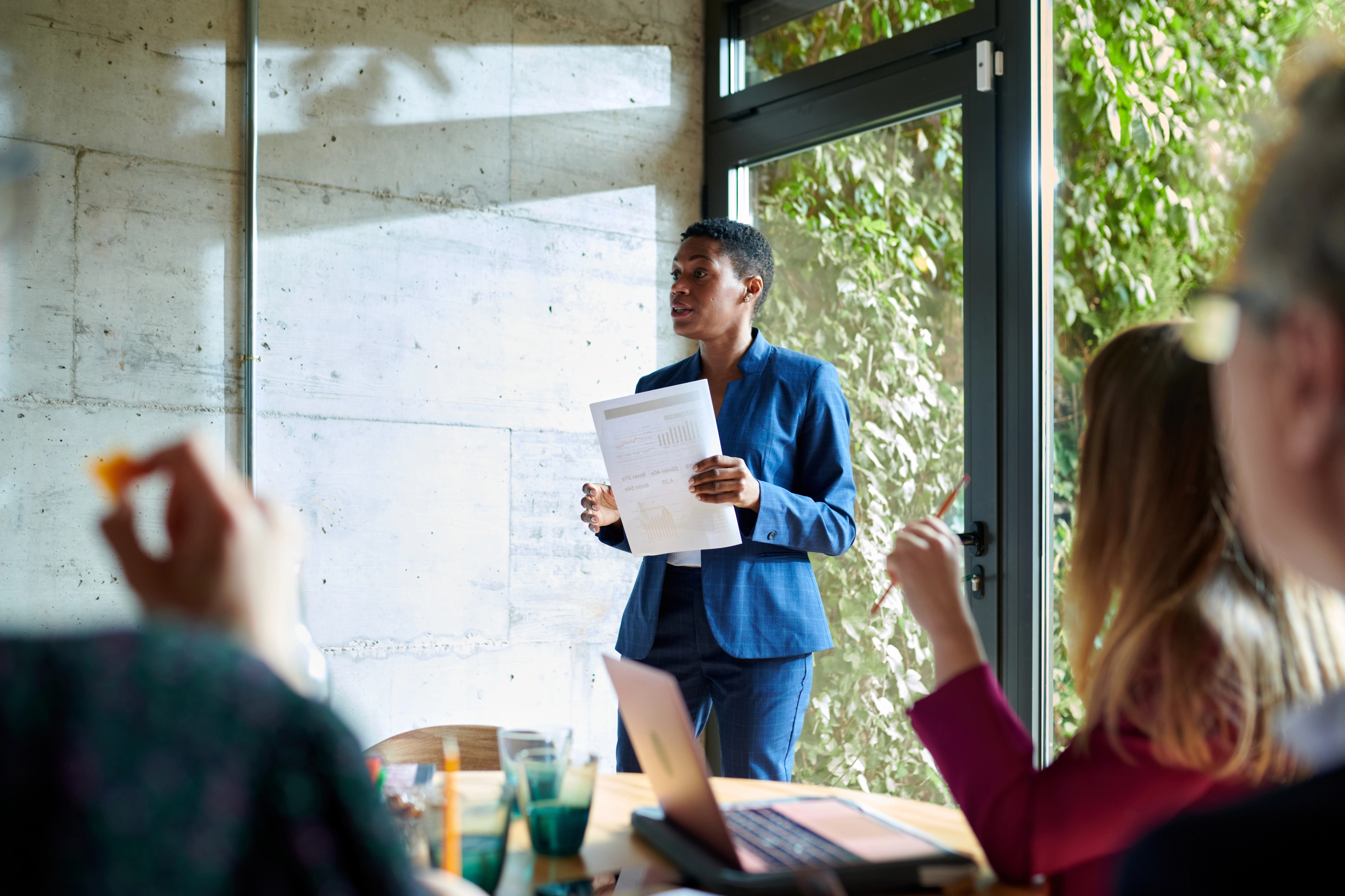 A businesswoman standing in front of a group of coworkers, presenting a document.
